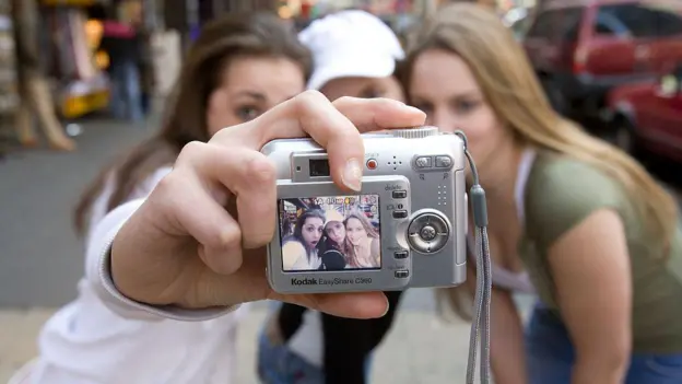 Persona revisando fotos antiguas en una cámara digital de los 2000, con expresion de sorpresa al descubrir recuerdos perdidos