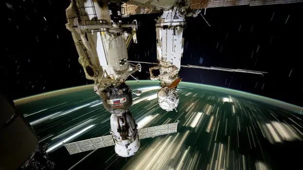 Estación Espacial Internacional orbitando la Tierra con paneles solares desplegados, vista desde la Cúpula con la Tierra al fondo iluminada por el sol
