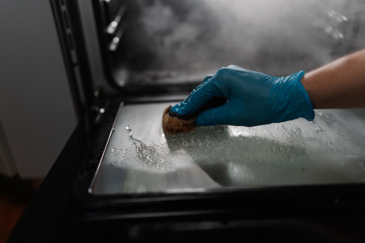 Mano aplicando pasta de bicarbonato y vinagre sobre el cristal del horno para eliminar grasa sin químicos agresivos
