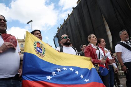 Manifestantes en Plaza Bolívar piden liberación de presos políticos en Venezuela, con carteles que exigen 'Democracia ya' bajo un cielo nublado