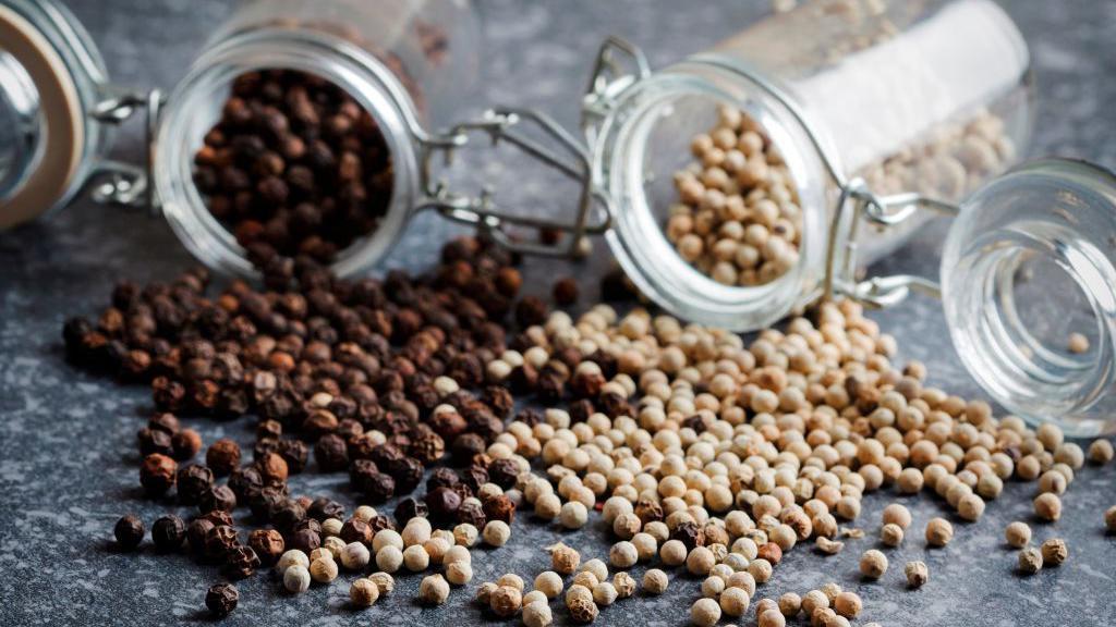Granos de pimienta negra molidos junto a vegetales frescos, mostrando cómo potencia la absorción de vitaminas y minerales en comidas saludables
