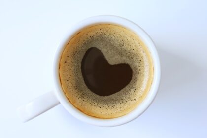 Taza de café negro humeante con granos de café alrededor, simbolizando los beneficios cardiovasculares y cognitivos respaldados por la ciencia