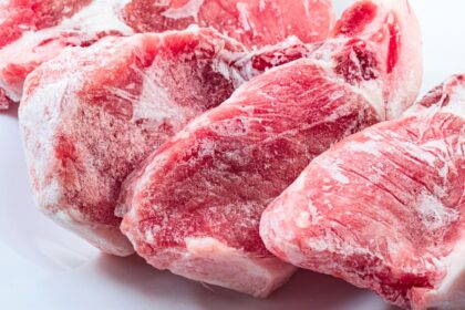 Tabla de cortar con carne fresca roja, frutas enteras y botella de agua cristalina, destacando frescura y calidad para una dieta saludable