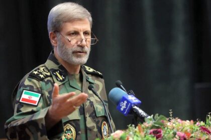 General iraní Amir Hatami en postura de alerta militar con mapa de Oriente Medio y flota estadounidense desplegada en el Golfo Pérsico