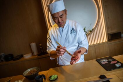 Chef preparando nigiri de Nodoguro ahumado con carbón binchotan en barra de madera de Kiwami, con vistas al East River