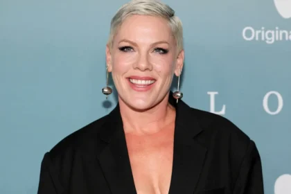 Pink sonriendo en una cama de hospital tras su cirugía cervical, mostrando su actitud positiva y resiliente