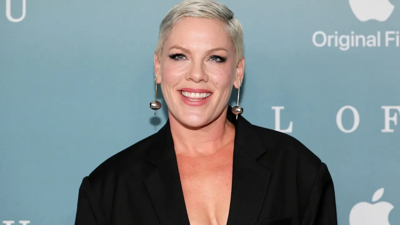 Pink sonriendo en una cama de hospital tras su cirugía cervical, mostrando su actitud positiva y resiliente