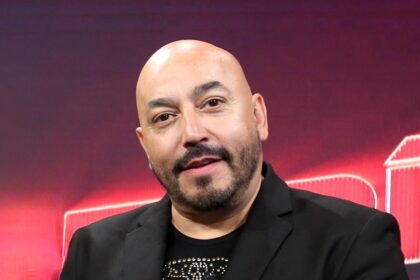 Lupillo Rivera explicando su estrategia clave para ganar en un reality show, con parejas compitiendo en un escenario de apuestas