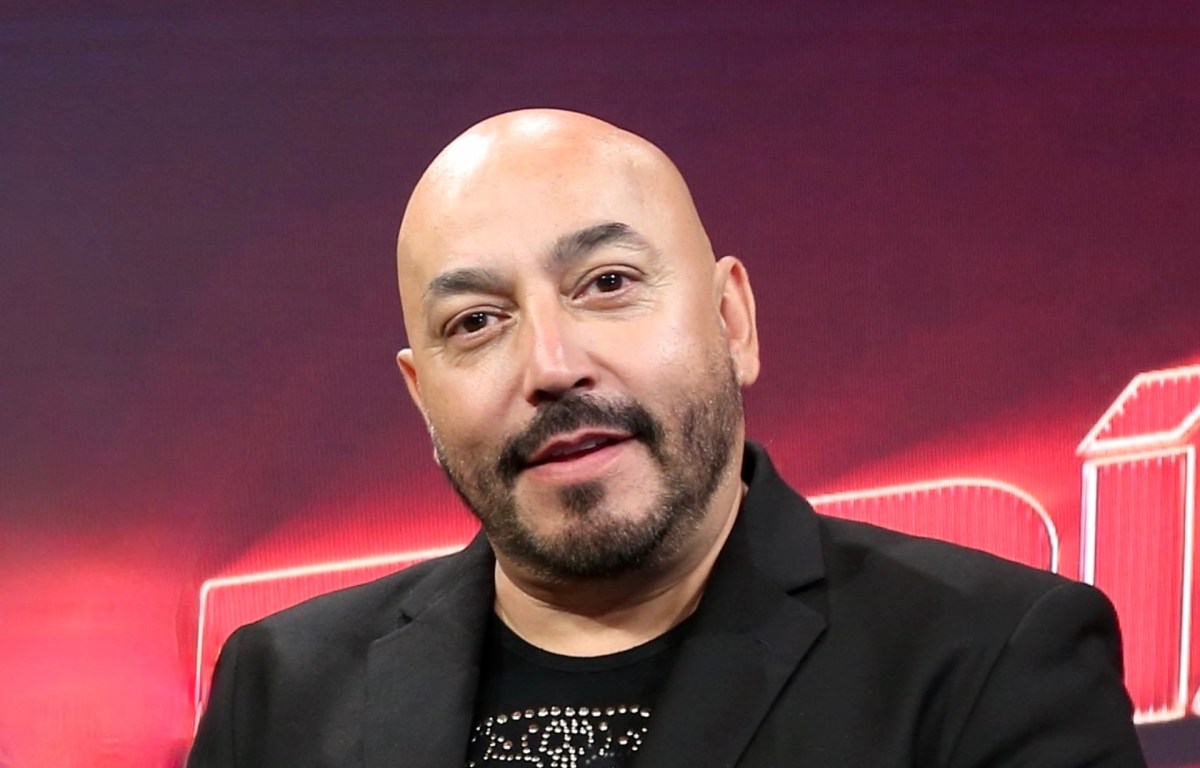 Lupillo Rivera explicando su estrategia clave para ganar en un reality show, con parejas compitiendo en un escenario de apuestas