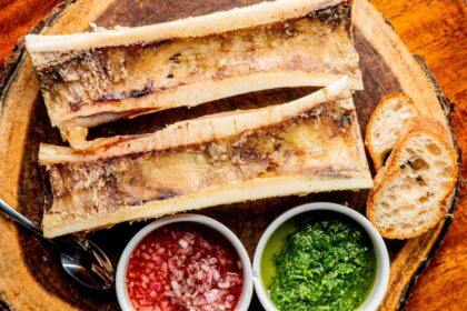 Rodajas de fémur de vaca con tuétano dorado al horno, mezclándose con mantequilla clarificada y hierbas frescas para crear un condimento umami