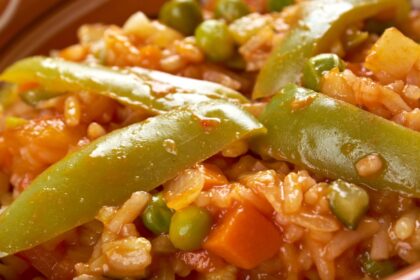 Plato de arroz caldoso con alitas de pollo doradas, alcachofas y zanahorias en rodajas, cocinado a presión para un grano meloso y lleno de sabor