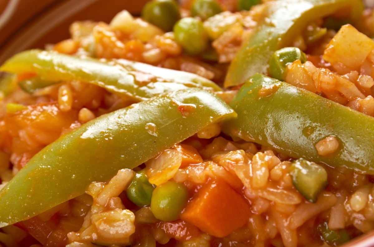 Plato de arroz caldoso con alitas de pollo doradas, alcachofas y zanahorias en rodajas, cocinado a presión para un grano meloso y lleno de sabor