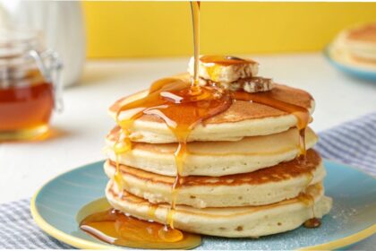 Plato con pancakes ilimitados de suero de leche, acompañados de jarabes de arándano, fresa, mantequilla y nuez, listos para disfrutar en el restaurante