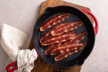 Tiras de bacon doradas y crujientes sobre rejilla en bandeja de horno, con grasa separada para menos absorción