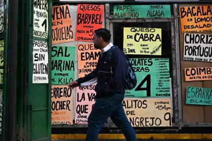 Mujer revisando precios en dólares en un supermercado venezolano con estantes semivacíos y billetes de bolívares devaluados en mano