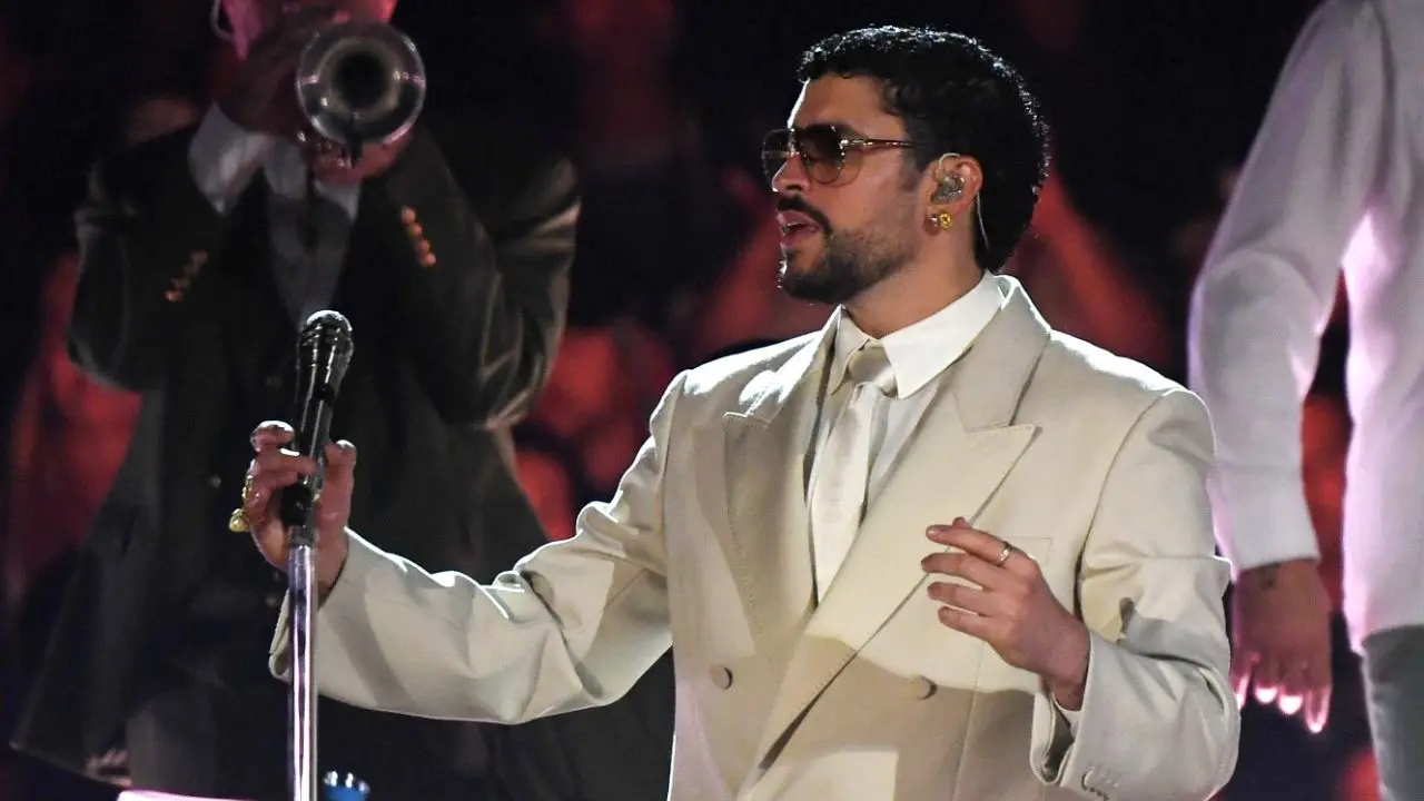 Bad Bunny en el escenario del Atanasio Girardot con traje beige oversize y sombrero de orejeras, interpretando éxitos ante un público con banderas de Puerto Rico y Colombia
