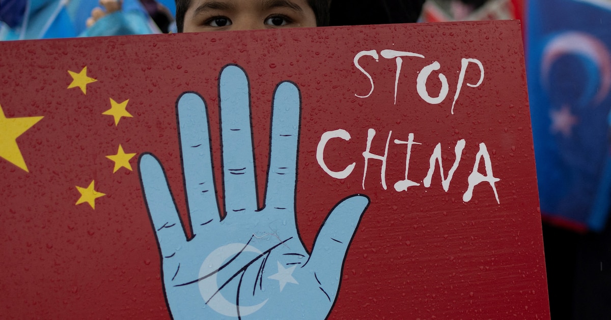 Grupo de uigures protestando con carteles contra la represión china en Xinjiang, rodeados de alambradas y vigilancia
