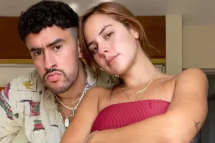 Bad Bunny y Gabriela Berlingeri sonriendo en una playa australiana durante la gira Debí Tirar Más Fotos, con gafas de sol y ropa casual.