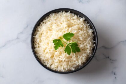 Arroz blanco cremoso con granos sueltos y brillantes, cocinado con caldo de pollo y mantequilla en una cacerola de acero inoxidable