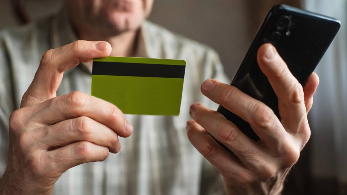 Persona con teléfono en mano recibiendo llamada sospechosa de estafa bancaria mientras revisa su app con alerta de transferencia fraudulenta
