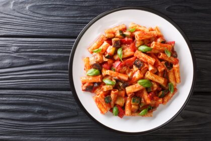 Plato de tortiglioni dorados mezclados con tiras de pimientos asados, berenjena y perejil fresco sobre bol de cerámica rústica