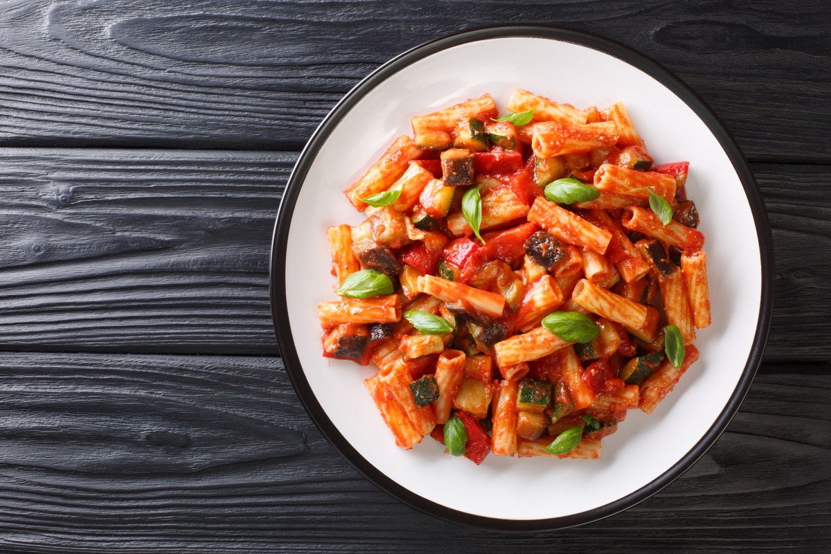 Plato de tortiglioni dorados mezclados con tiras de pimientos asados, berenjena y perejil fresco sobre bol de cerámica rústica