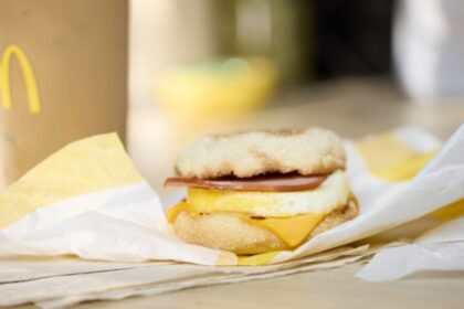 Sándwich Egg McMuffin abierto mostrando huevo fresco, tocineta canadiense y queso americano fundido sobre muffin tostado