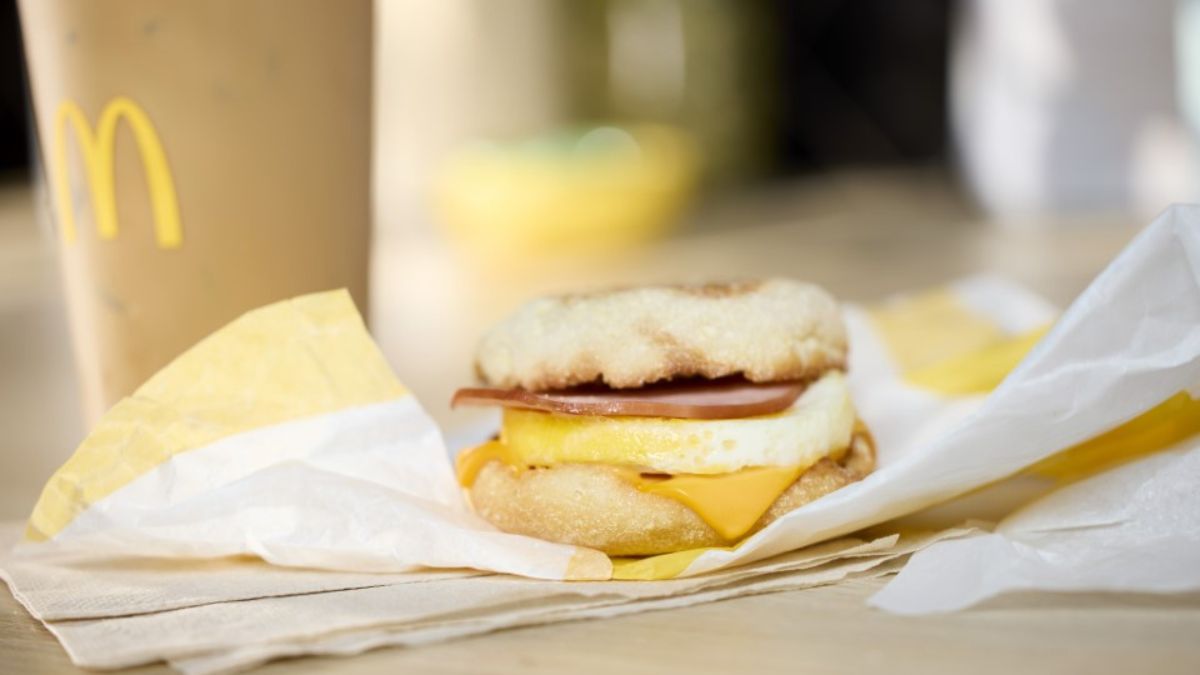 Sándwich Egg McMuffin abierto mostrando huevo fresco, tocineta canadiense y queso americano fundido sobre muffin tostado