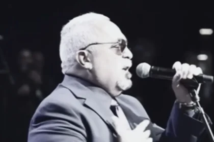Willie Colón tocando el trombón en un escenario, rodeado de músicos, con expresión intensa y pasión por la salsa