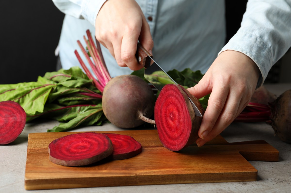 Espinacas, tomates, acelgas y remolachas crudas en una mesa de cocina con etiquetas de advertencia sobre potasio y oxalatos para riñones