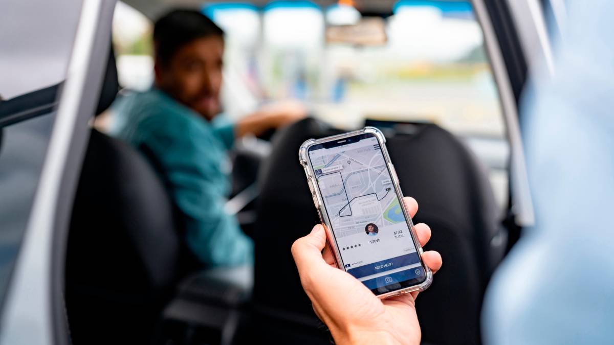Conductor de plataforma de movilidad revisando su teléfono con expresión de preocupación por multas de $4.7 millones por viaje en Colombia