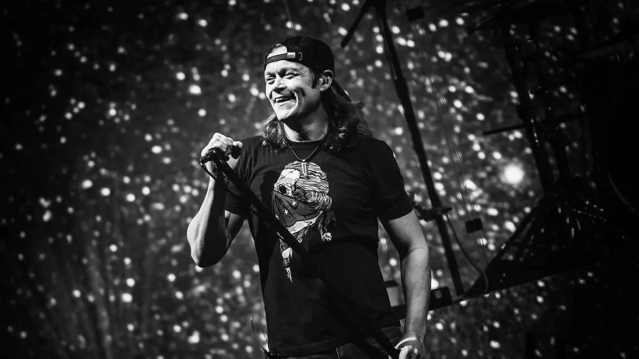 Brad Arnold cantando 'Kryptonite' en un concierto masivo de 3 Doors Down ante 50.000 fans, con su característico micrófono en mano y luces de escenario al fondo