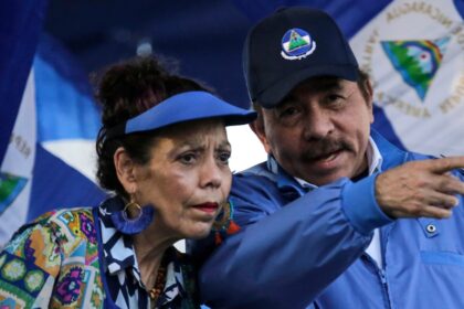 Daniel Ortega y Rosario Murillo en un acto oficial con banderas de Nicaragua, simbolizando el control familiar del poder en medio de represión y exilio masivo