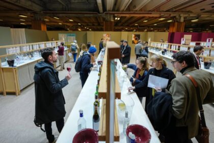 Copa de vino sin alcohol en el Salón del Vino de París, rodeada de etiquetas con lemas como 'sin alcohol, sin remordimientos' para adultos jóvenes