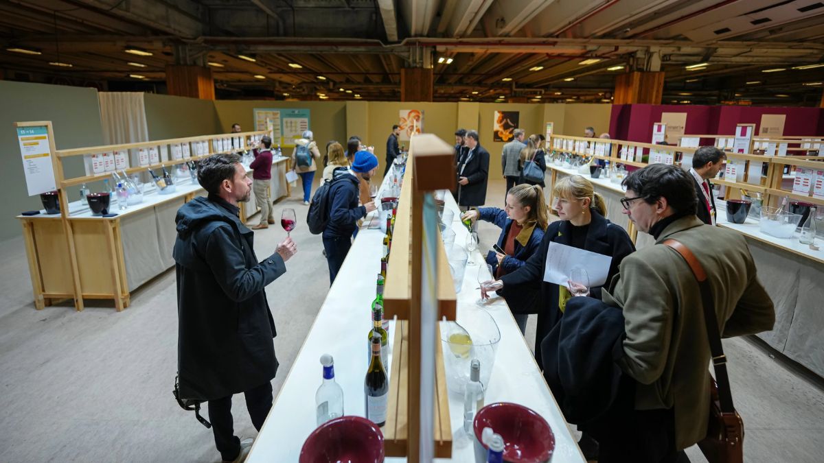 Copa de vino sin alcohol en el Salón del Vino de París, rodeada de etiquetas con lemas como 'sin alcohol, sin remordimientos' para adultos jóvenes