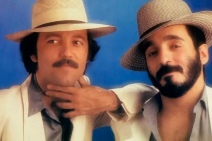 Rubén Blades y Willie Colón en un escenario oscuro, iluminados por un foco, con partituras de 'El Baquiné de los Angelitos Negros' al fondo