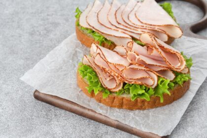 Rebanada de jamón de pavo procesado con etiqueta de alto contenido en sodio y nitritos, junto a advertencia de riesgo cancerígeno según la OMS