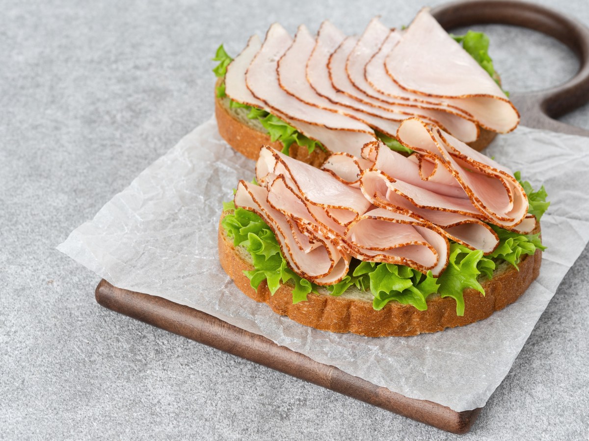 Rebanada de jamón de pavo procesado con etiqueta de alto contenido en sodio y nitritos, junto a advertencia de riesgo cancerígeno según la OMS
