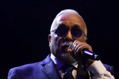 Willie Colón tocando el trombón en un escenario neoyorquino, rodeado de luces que reflejan su influencia en la salsa moderna
