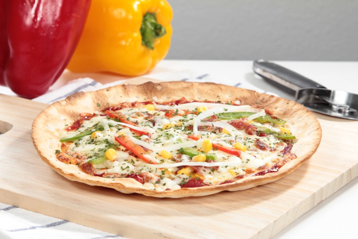 Tortilla pizza dorada con queso fundido, tomates frescos y cilantro, servida en plato blanco con tenedor