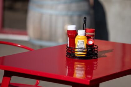 Ingeniera en alimentos señalando latas y aderezos contaminados en un restaurante, mostrando riesgos al comer fuera