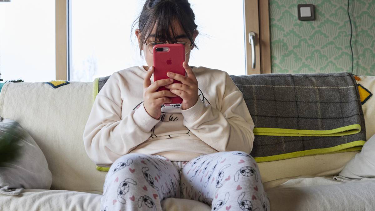 Niño con expresión de ansiedad mirando fijamente una tablet con redes sociales abiertas mientras ignora un balón de fútbol en el suelo