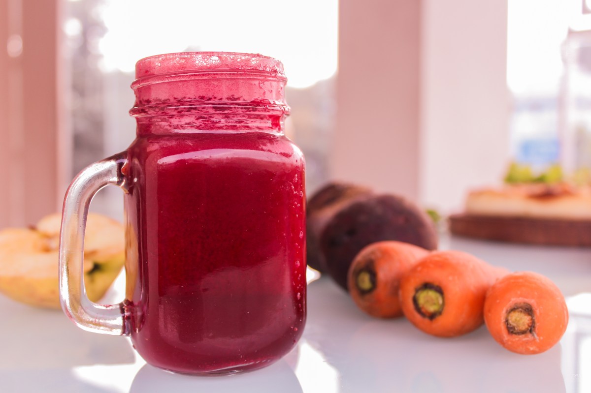 Vaso de jugo de remolacha vibrante con trozos frescos alrededor y fondo de estudio científico sobre presión arterial