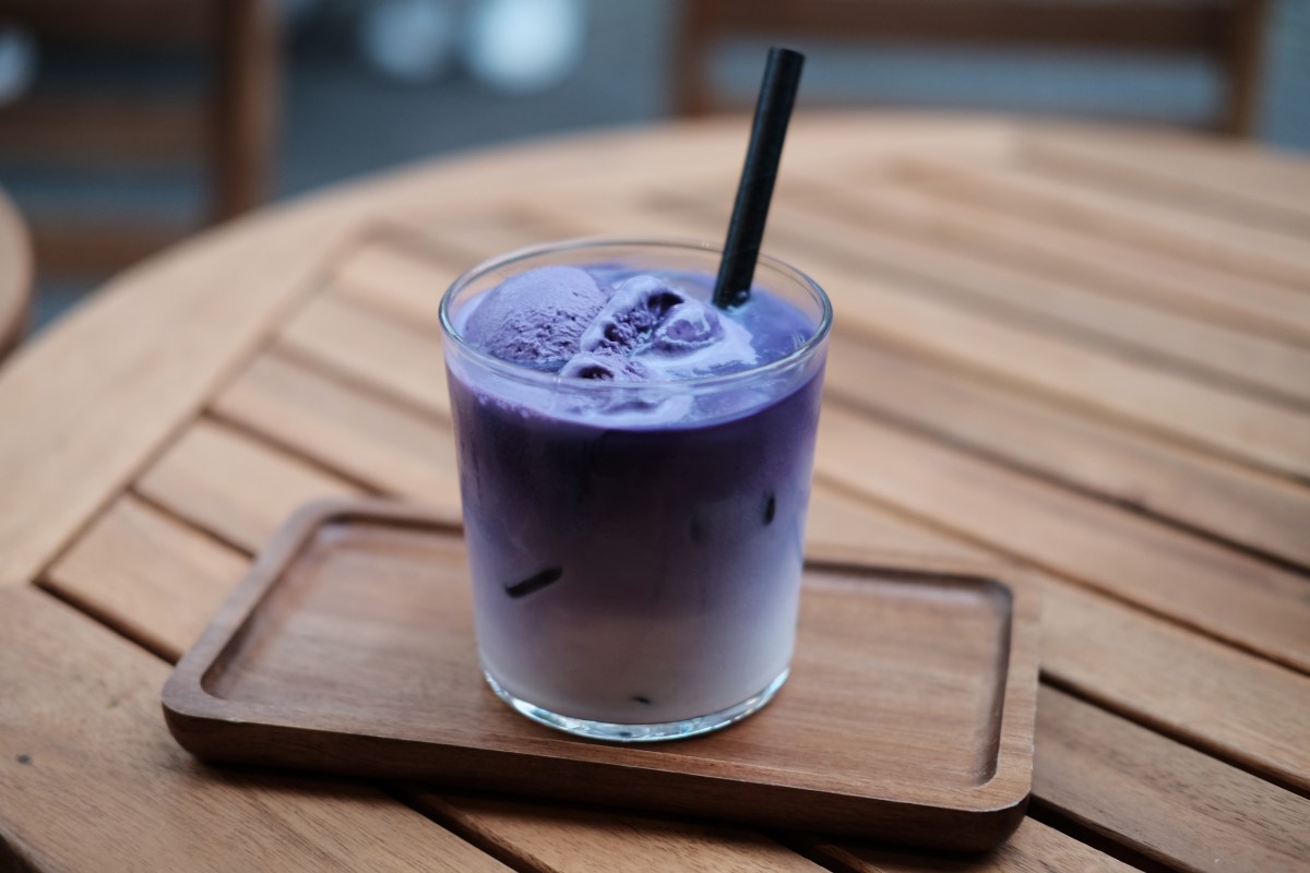 Vaso de Ube Latte con espuma cremosa y tono lila intenso por el ñame morado, decorado con canela en polvo sobre mesa de madera