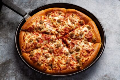 Chef italiana mostrando una pizza recién recalentada con base dorada y crujiente, queso derretido elástico y bordes perfectos usando su técnica de sartén y vapor