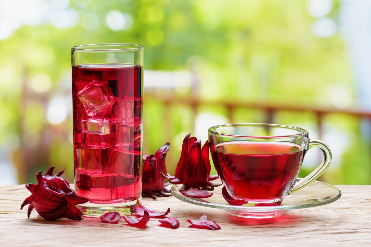 Taza de té rojo de flor de Jamaica con cálices secos alrededor, destacando su color intenso y propiedades antioxidantes para la presión arterial