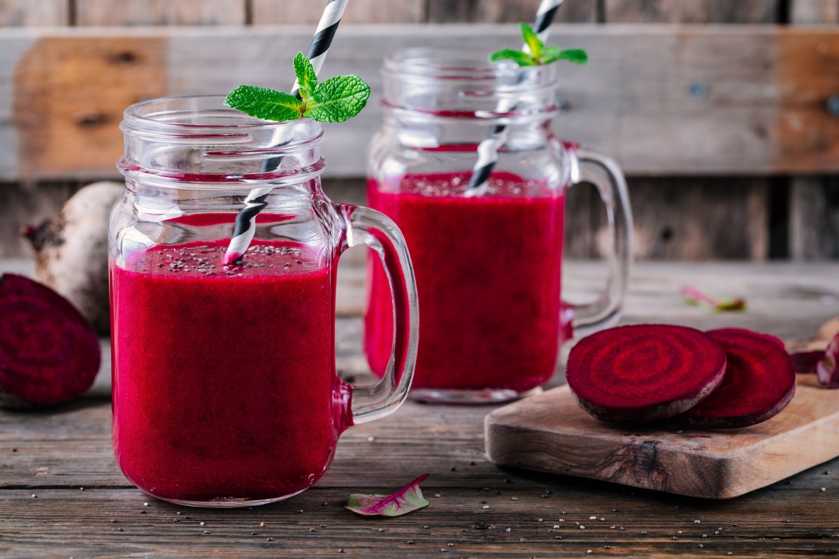 Vaso de jugo de remolacha fresco con rodajas del tubérculo morado sobre mesa de madera, mostrando su intenso color natural