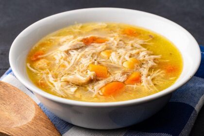 Tazón humeante de caldo tradicional dorado con hierbas y trozos de pollo, símbolo de reconfort y tradición culinaria en cada cultura