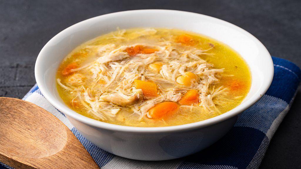 Tazón humeante de caldo tradicional dorado con hierbas y trozos de pollo, símbolo de reconfort y tradición culinaria en cada cultura