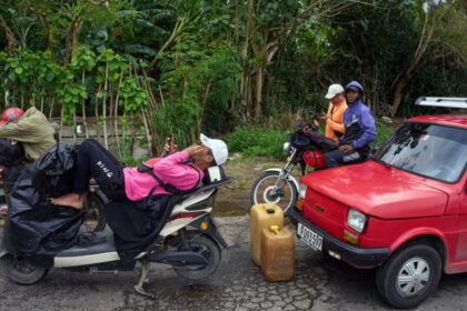 Fila de autos bajo el sol en Cuba esperando gasolina durante apagón de 16 horas con edificios oscuros al fondo